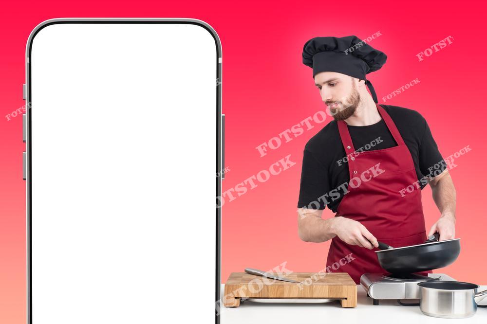 Фото демонстрирует концепцию заказа еды из ресторана с помощью смартфона. Фотография показывает мужчину-повара, держащего телефон с белым пустым экраном, предназначенным для размещения шаблона приложения доставки. Фотоснимок передаёт идею оформления заказа, сервиса доставки и работы ресторанного повара, готовящего блюдо на фоне закатного настроения. Изображение подчёркивает современный формат ресторанного обслуживания и цифровые технологии.